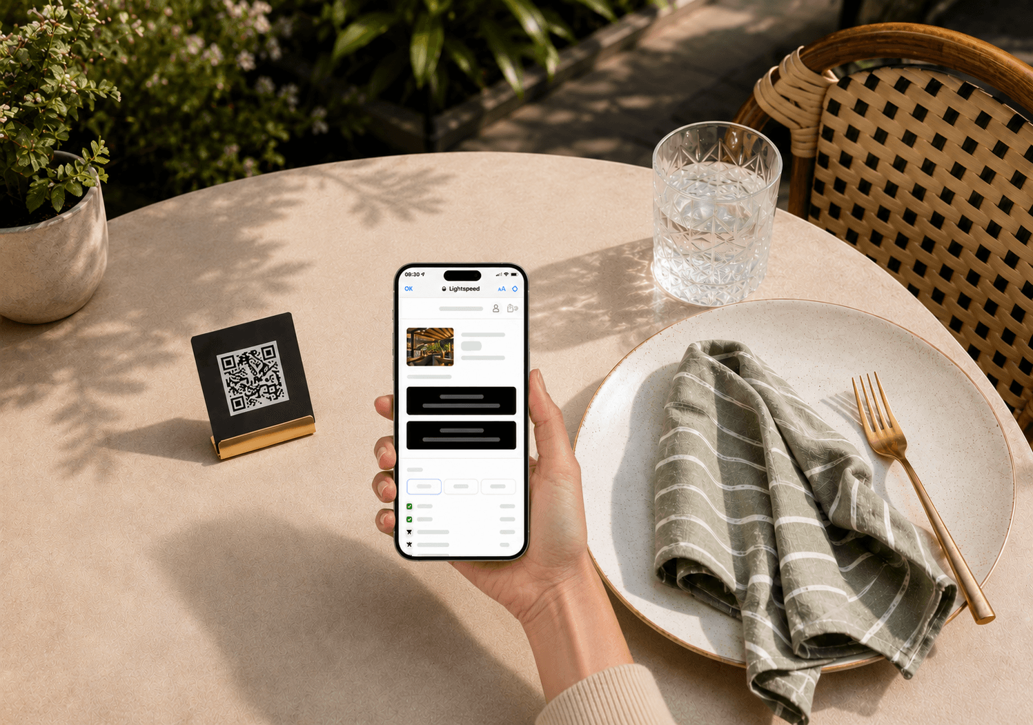 Hand hält ein Smartphone mit digitaler Bezahloberfläche an einem gedeckten Tisch auf einer sonnigen Restaurantterrasse mit QR Code.