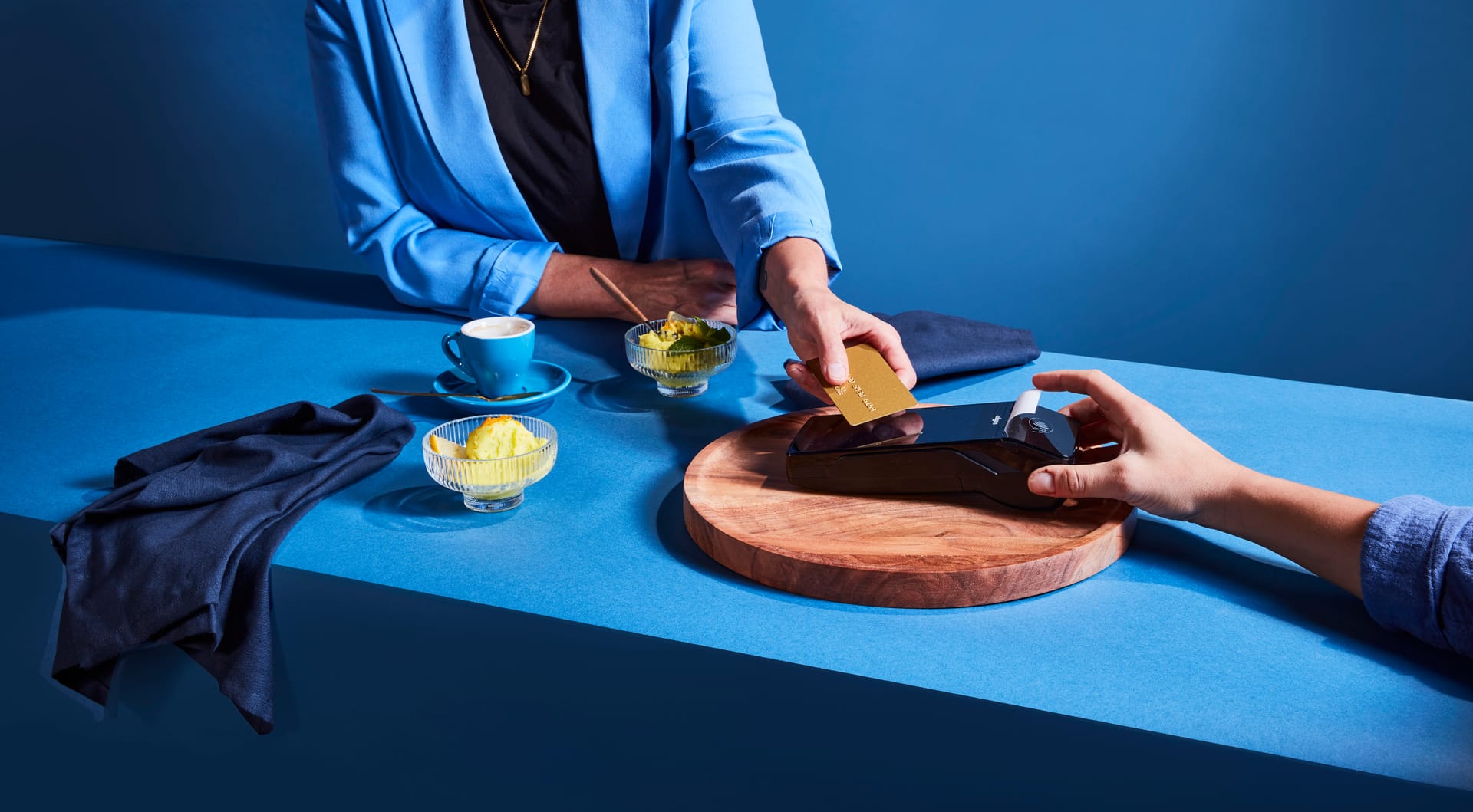 Gast bezahlt kontaktlos am Tisch mit Karte ueber ein modernes Kartenterminal. Auf dem Tisch stehen Espresso und Dessert. Szene vermittelt effiziente, nahtlose Zahlung im Gastronomiealltag.